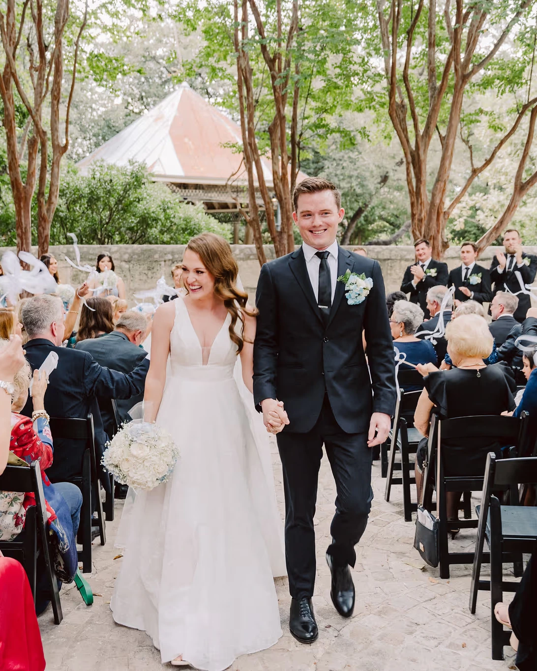 A couple walks back up the aisle as guests wave white ribbons